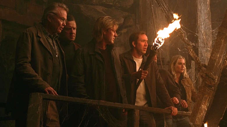 Ben and company walk through an underground passage with a torch in National Treasure (2004)