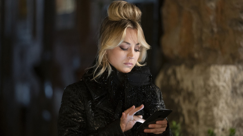 Cassie looking at her phone in a black sparkly coat on The Flight Attendant