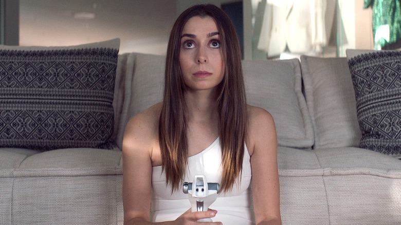 Hazel sitting against a white couch in "Made for Love."