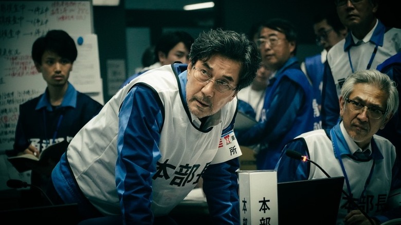 Yoshida leans over a console as a crowd of staffers behind him scrambles in The Days