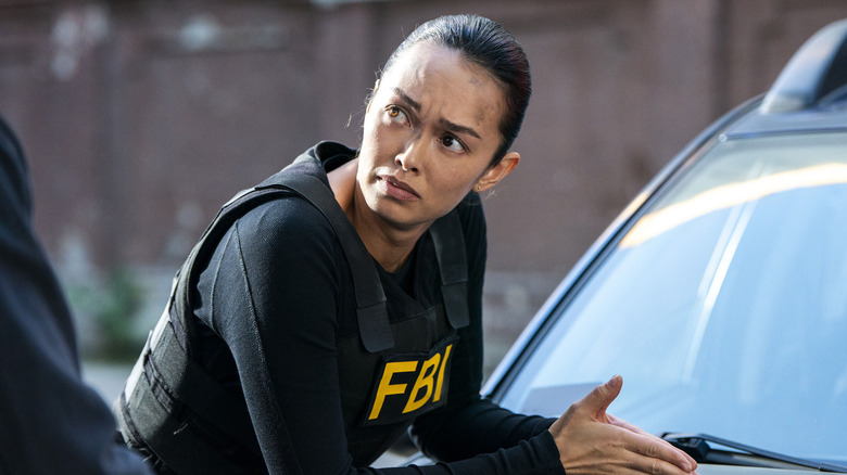 Cameron leans over the hood of a car in FBI: International