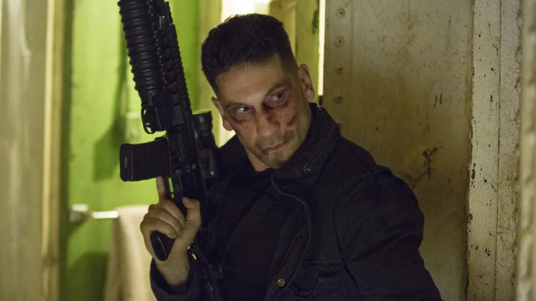 Frank holds a machine gun and peers around a corner in Punisher