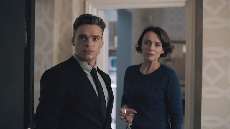 Budd stands at the door in front of Montague holding a glass of wine in Bodyguard