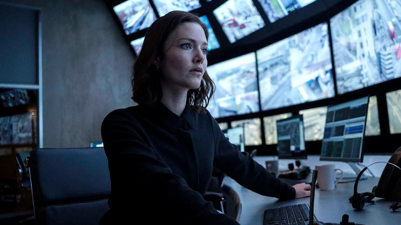 Carey sits at a control room desk in front of a dozen monitors in The Capture