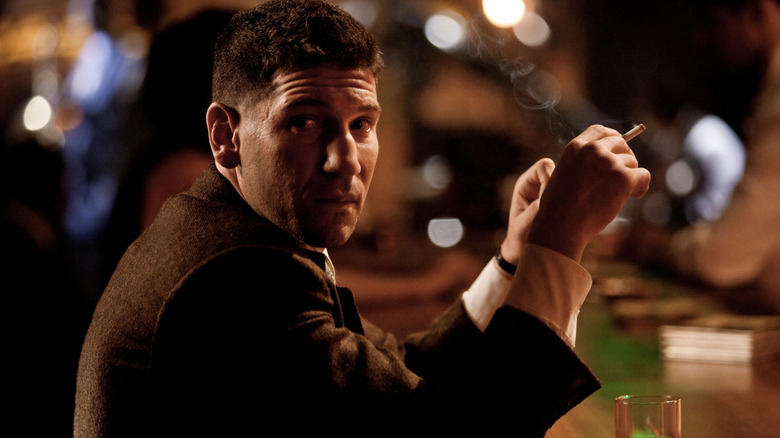 Teague sits at a bar smoking a cigarette