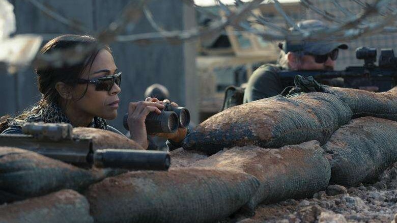 Joe peers over sandbags with binoculars in Lioness