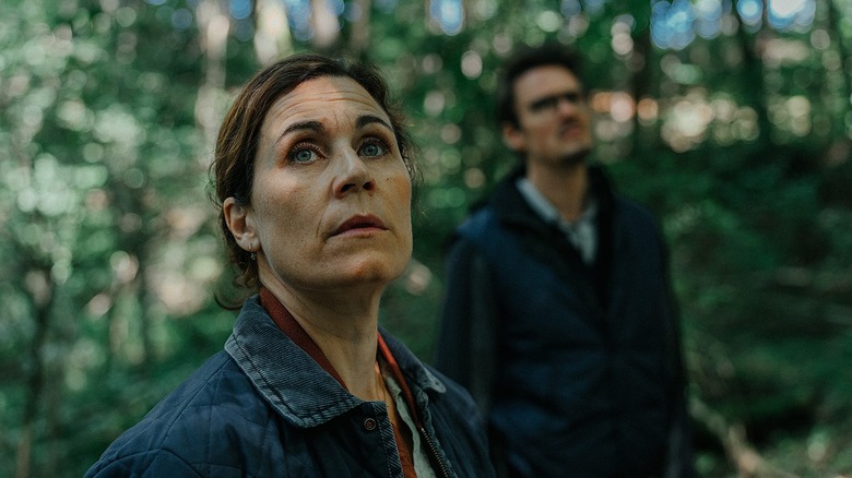 Barbara and Thomas stand in the woods looking up in "The Black Forest Murders" (2025)