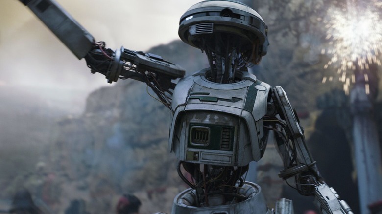 The silver droid L3-37 raises a fist in a call to revolution as a blaster bolt explodes behind her in "Solo"