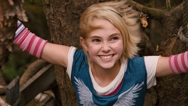 Leslie raises her arms and smiles in a tree