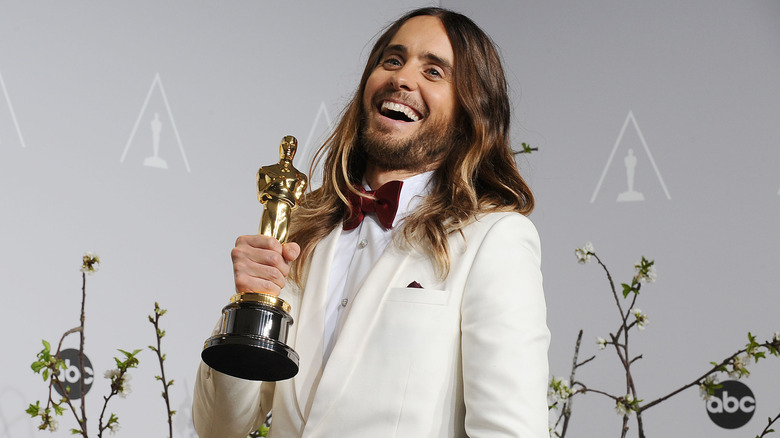 Jared Leto posing for cameras with his academy award while standing in front of the post-show backdrop from ABC