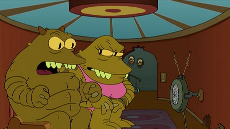 Lrrr sitting in front of the TV with his fists clenched in anger next to his wife Ndnd in "Futurama"