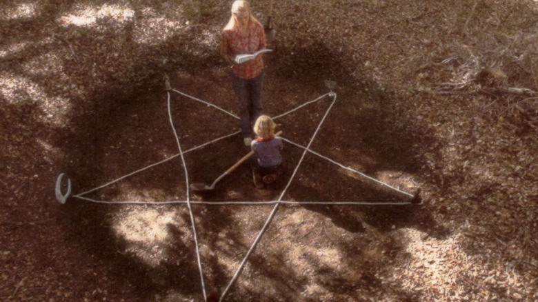 Oralee and Nathan stand in a wooded area marked with a pentagram in "Antrum" (2018)