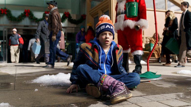 Jake sitting on a sidewalk outside of a store in "8-Bit Christmas" (2021)