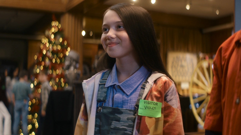 Violet smiling with a Christmas tree in the background in "A Christmas Mystery" (2022)