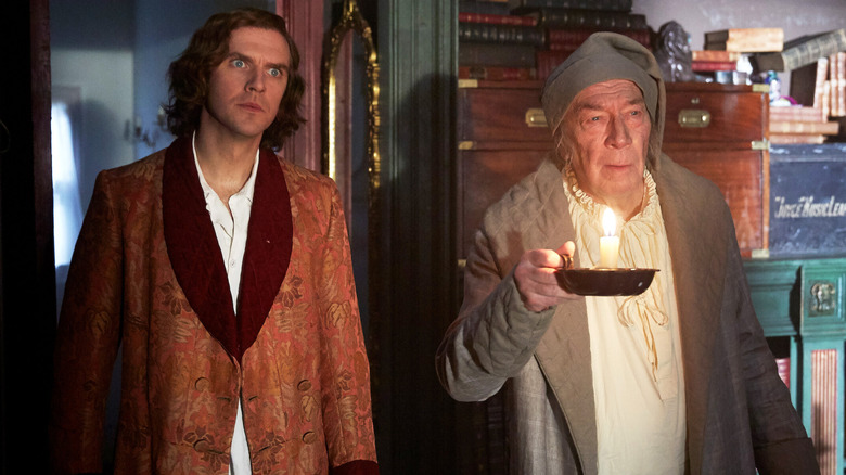 Charles Dickens stands near Ebenezer Scrooge holding a candle in "The Man Who Invented Christmas" (2017)