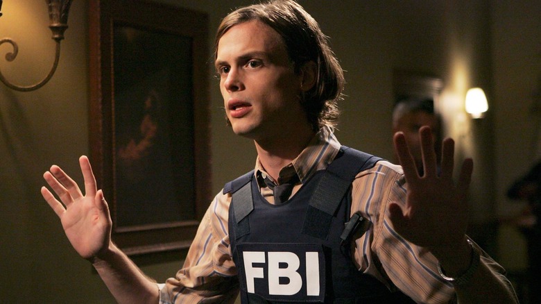 Spencer Reid holding his hands up while wearing an FBI bullet-proof vest