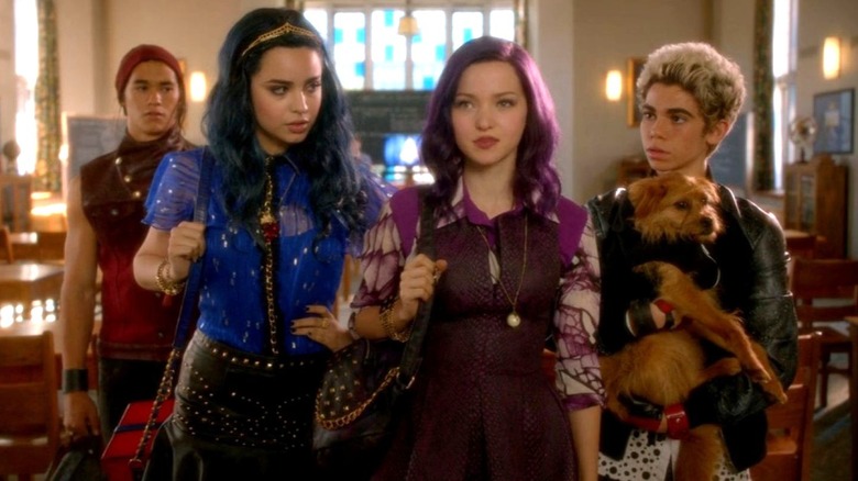 Jay stands behind Evie, Mal, and Carlos, who is holding a dog in Descendants