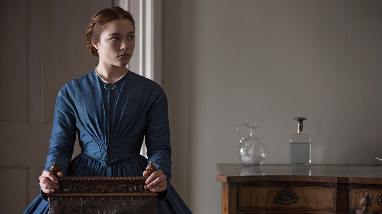 Katherine standing behind the chair in a large dress in Lady Macbeth