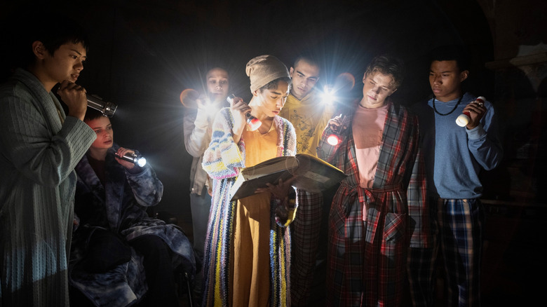 Teens with flashlights looking at book in The Midnight Club