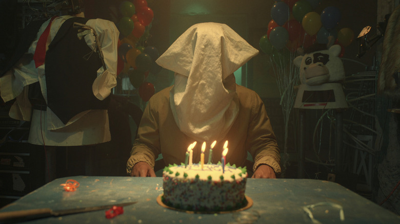 A man sits at a table with a bag over his head in Them