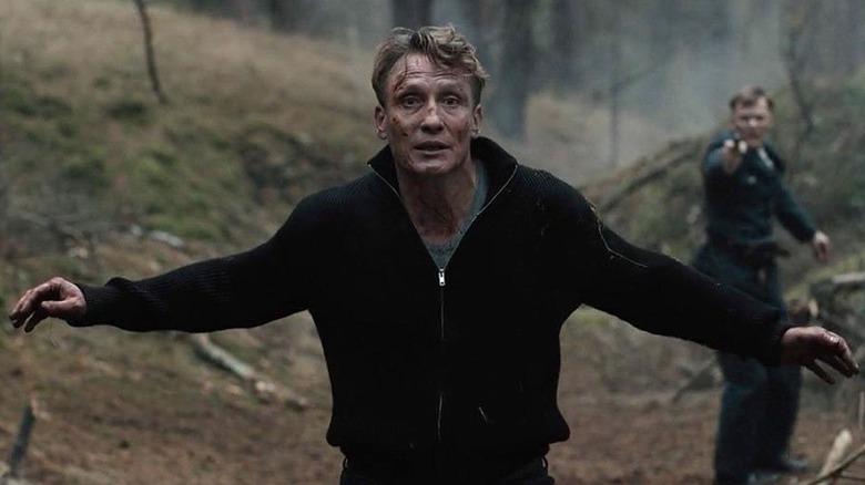 Ulrich raises his arms while a gunman aims a pistol behind him in Dark.