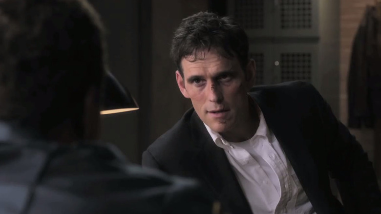 Ethan sits behind a desk talking to someone in Wayward Pines.