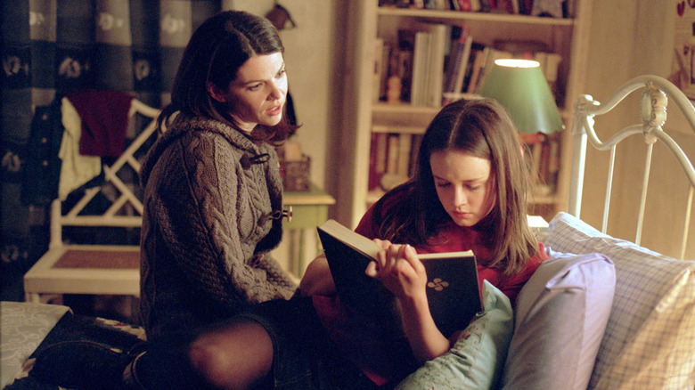 Lorelai sitting on Rory's bed while Rory reads a book on Gilmore Girls