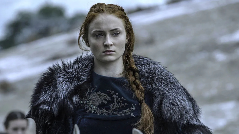 Sansa Stark sitting on horseback in a winter gown embroidered with a dire wolf, the snowy, gray winter landscape behind her