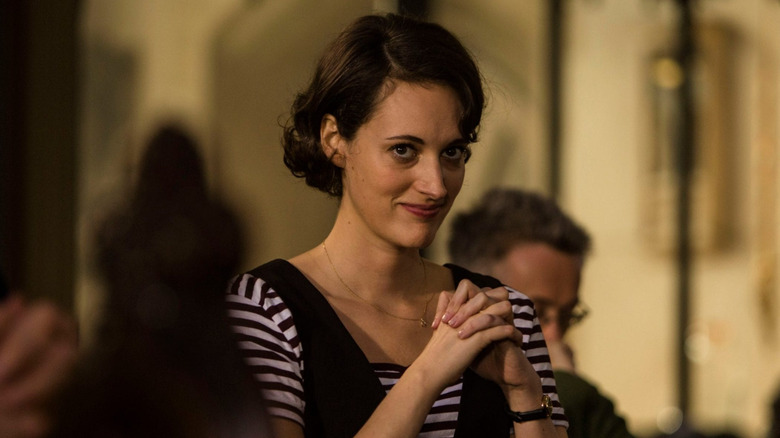 Fleabag (Phoebe Waller-Bridge) smirking and holding her hands together in prayer at a service given by the Hot Priest