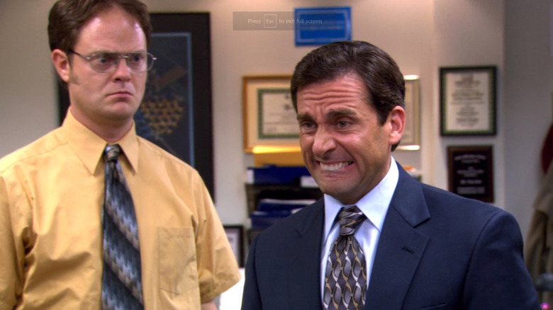 Dwight angrily staring at Michael as Michael bites his lower lip and wrinkles his forehead after saying something he regrets