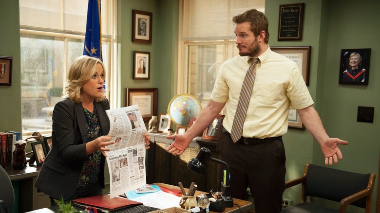 Leslie holding up a newspaper with Andy in her office on Parks and Recreation