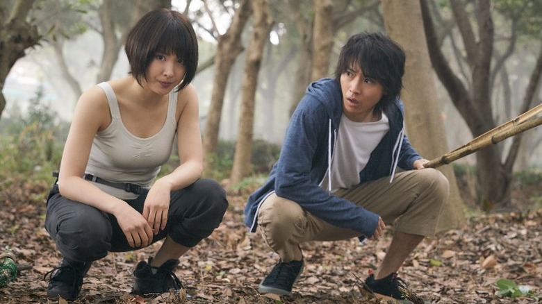 Usagi and Arisu crouch down in a forest on "Alice in Borderland" (2020-present)