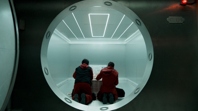 Two robbers in red kneel before a stack of money inside a safe in "Money Heist" (2017-2021)