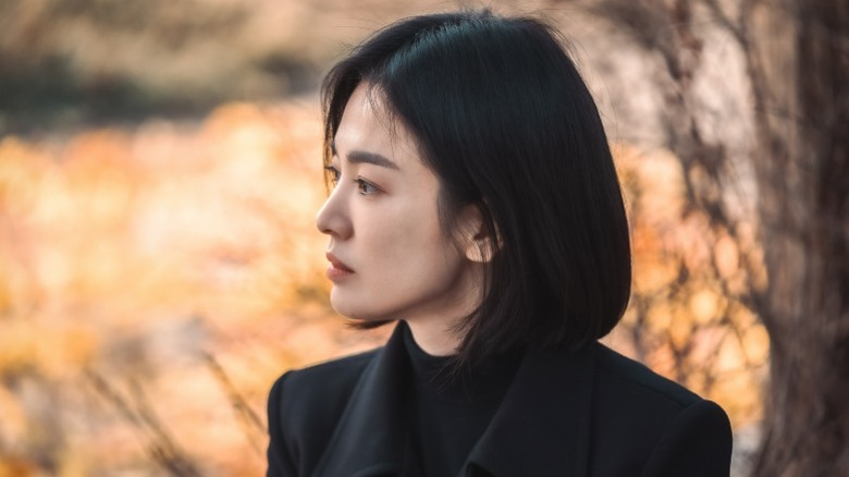 Dong-eun dressed in black stands next to a tree on "The Glory" (2022-2023)