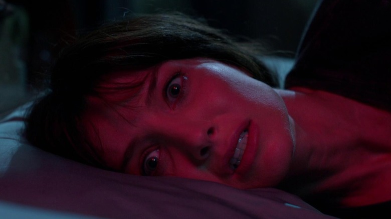 Madison laying in bed bathed in red light in Malignant