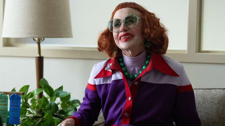 Gladys smiling with green glasses in Marcus' office on Weapons