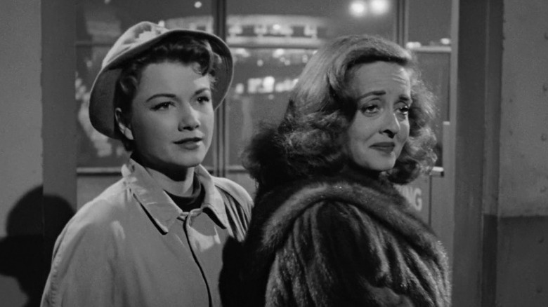 Eve Harrington and Margo Channing standing together and smiling lightly in All About Eve