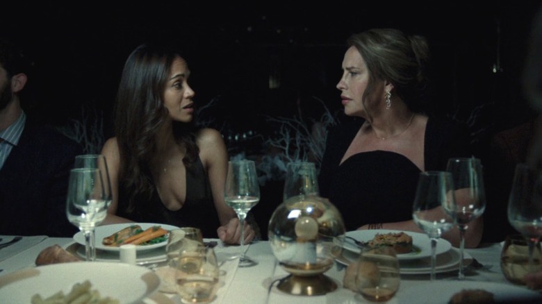 Rita Mora Castro and Emilia Pérez sitting side-by-side at a table and locking eyes in Emilia Pérez