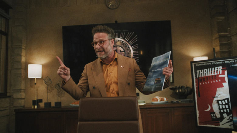 Matt Remnick holds a movie poster while standing behind a brown office chair in a brown and yellow suit in 