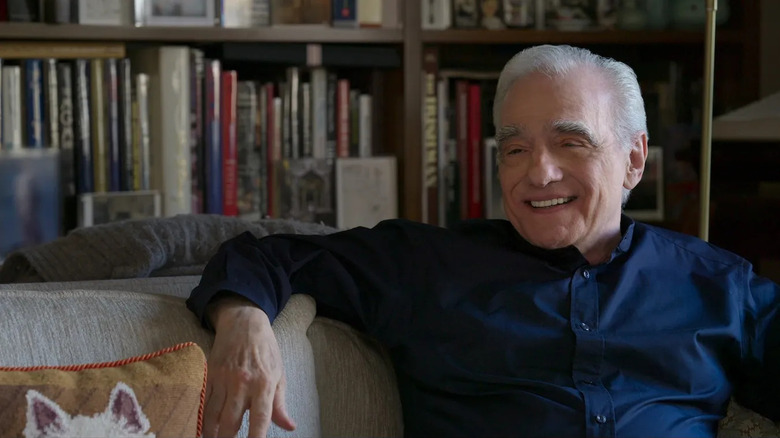 Martin Scorsese reclines on a white couch while smiling and wearing a blue shirt in "Mr. Scorsese"