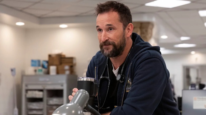Dr. Robby holds a metal coffee mug with his eyebrows raised on The Pitt