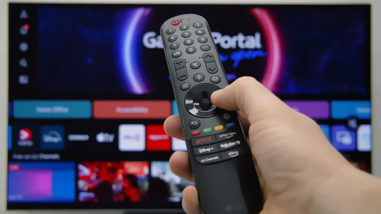 Hand holding LG TV remote pointing to webOS home screen