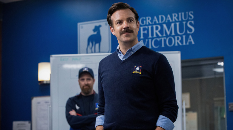 Ted smiling with Coach Beard behind him in Ted Lasso