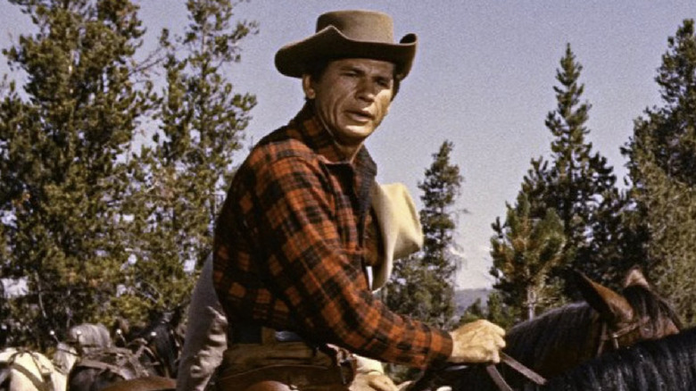 Reb wearing a red checkered shirt and a cowboy hat on a horse in "Jubal" (1956)