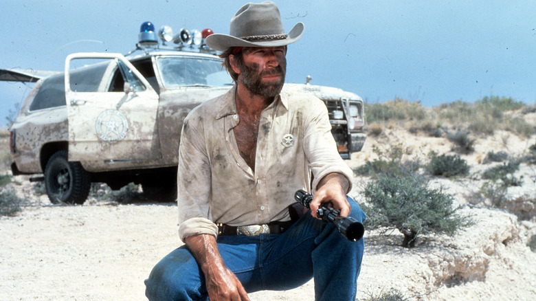 McQuade in dirty clothes squatting near a police car in "Lone Wolf McQuade" (1983)