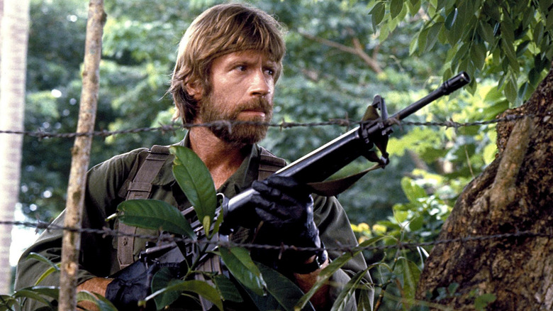 Braddock holding a gun near some barbed wire in "Missing in Action" (1984)