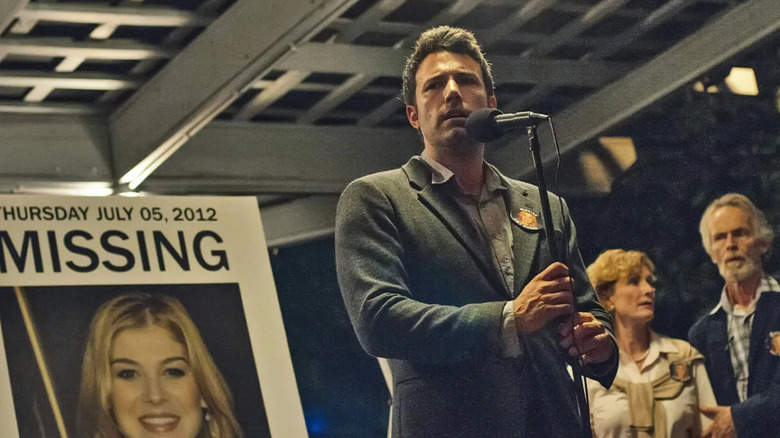 Nick in front of a missing poster delivering a speech in Gone Girl