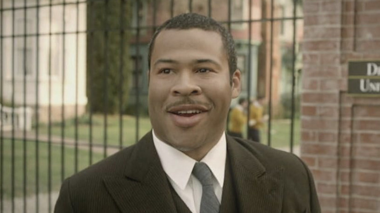 Percy smiling in front of a campus in "Drunk History"