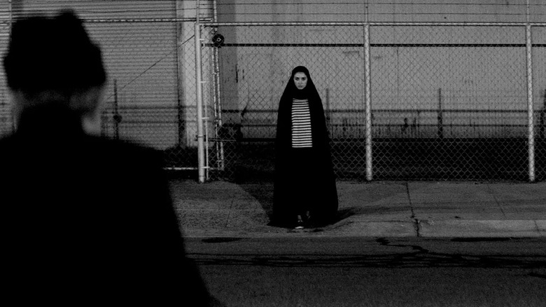 A strange young woman stands ominously on a sidewalk in A Girl Walks Home Alone At Night