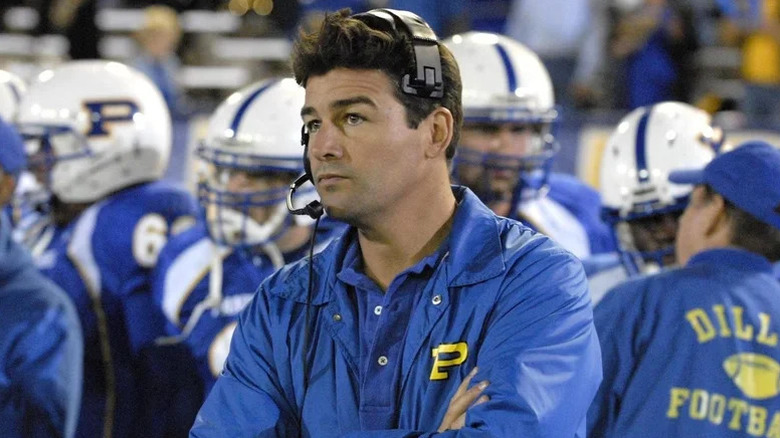 Eric Taylor looking thoughtful and surrounded by his team on Friday Night Lights